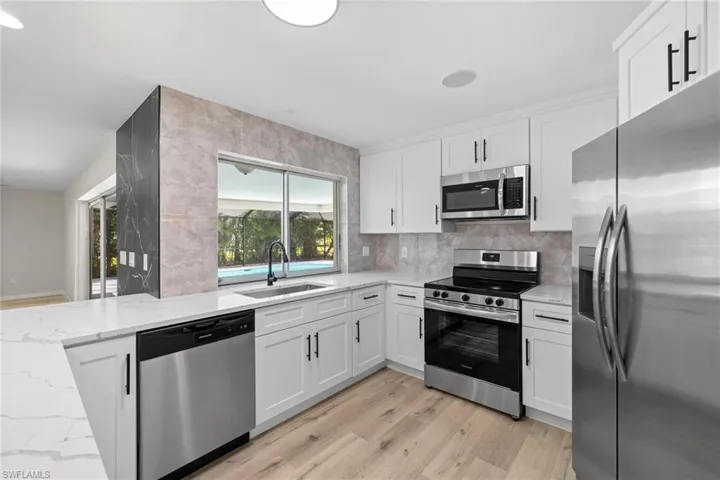 Kitchen featuring stainless steel appliances, light wood-type flooring, light stone counters, white cabinets, and tasteful backsplash