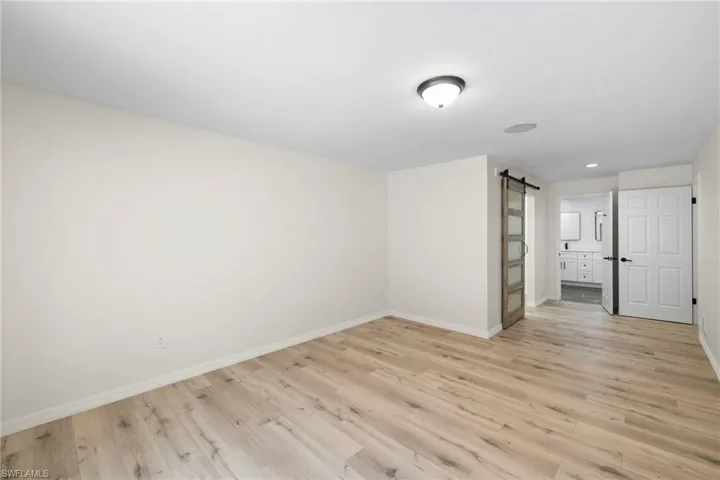 Unfurnished bedroom featuring a barn door, light wood-style flooring, ensuite bathroom, and recessed lighting