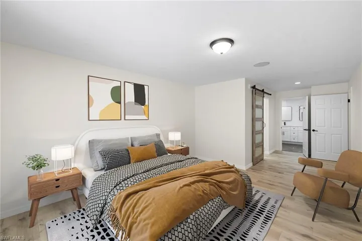 Bedroom featuring a barn door, light wood-type flooring, recessed lighting, and ensuite bath