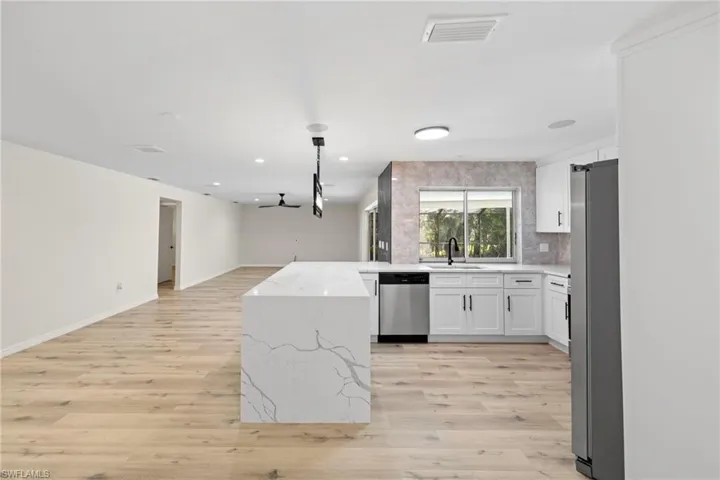 Kitchen with open floor plan, appliances with stainless steel finishes, light wood finished floors, white cabinets, and recessed lighting