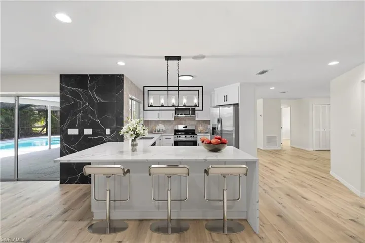 Kitchen featuring appliances with stainless steel finishes, recessed lighting, a breakfast bar, light stone countertops, and white cabinetry
