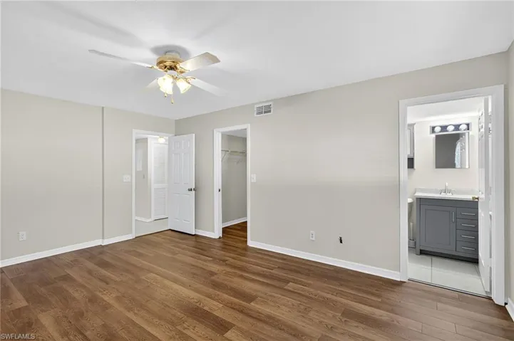 Unfurnished bedroom featuring wood finished floors, a spacious closet, a ceiling fan, and ensuite bathroom