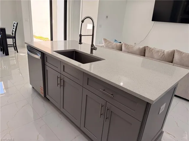 Kitchen with a kitchen island with sink, light stone countertops, dishwasher, open floor plan, and light marble finish flooring