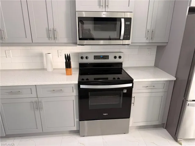 Kitchen with stainless steel appliances, gray cabinets, light stone counters, and light marble finish flooring