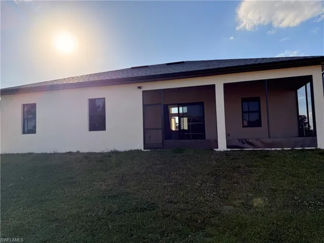 Rear view of property with a lawn, a sunroom, stucco siding, and a shingled roof