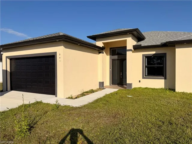 View of front of home with stucco siding, a front lawn, a garage, and concrete driveway