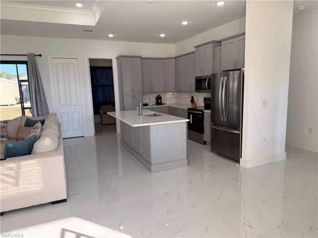 Kitchen with gray cabinetry, appliances with stainless steel finishes, a center island with sink, tasteful backsplash, and recessed lighting