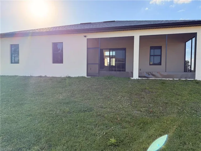 Back of house with a lawn, stucco siding, a sunroom, and a shingled roof