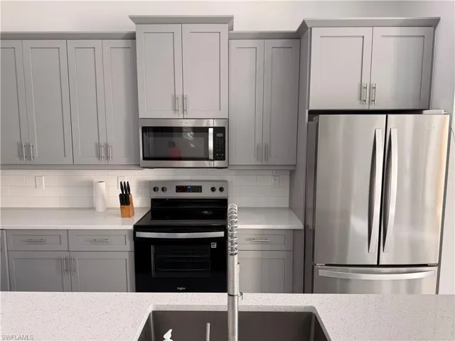Kitchen featuring gray cabinets, appliances with stainless steel finishes, and light stone counters