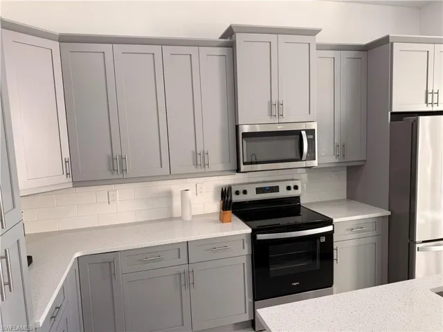 Kitchen with gray cabinets, appliances with stainless steel finishes, tasteful backsplash, and light stone countertops