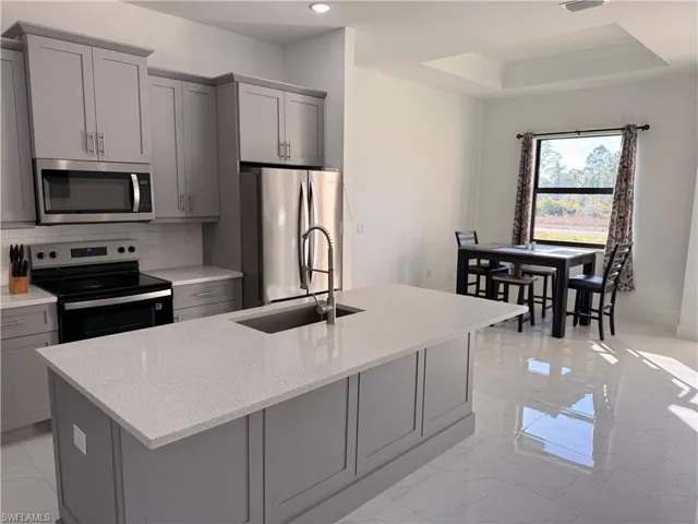 Kitchen featuring gray cabinetry, stainless steel appliances, light stone counters, tasteful backsplash, and ornamental molding
