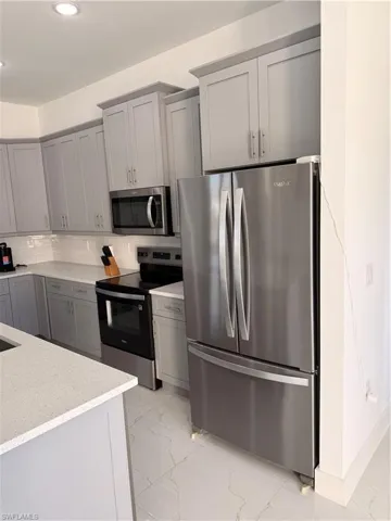 Kitchen featuring stainless steel appliances, gray cabinetry, light marble finish floors, light stone counters, and decorative backsplash
