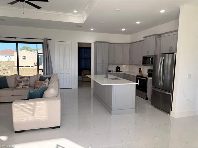 Kitchen with gray cabinets, stainless steel appliances, open floor plan, recessed lighting, and a center island with sink