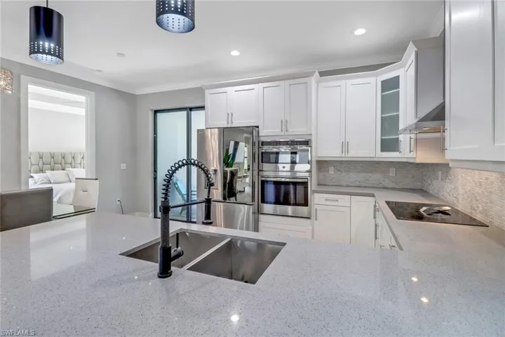 Kitchen featuring white cabinetry, hanging light fixtures, appliances with stainless steel finishes, decorative backsplash, and sink
