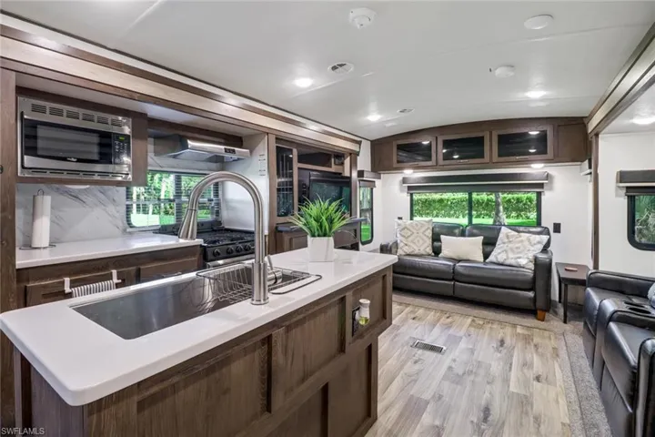 Kitchen featuring lofted ceiling, stainless steel microwave, dark brown cabinets, light wood-type flooring, and sink