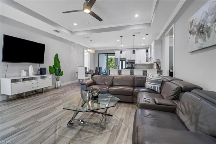 Living room with light hardwood / wood-style flooring, ceiling fan, a raised ceiling, and crown molding