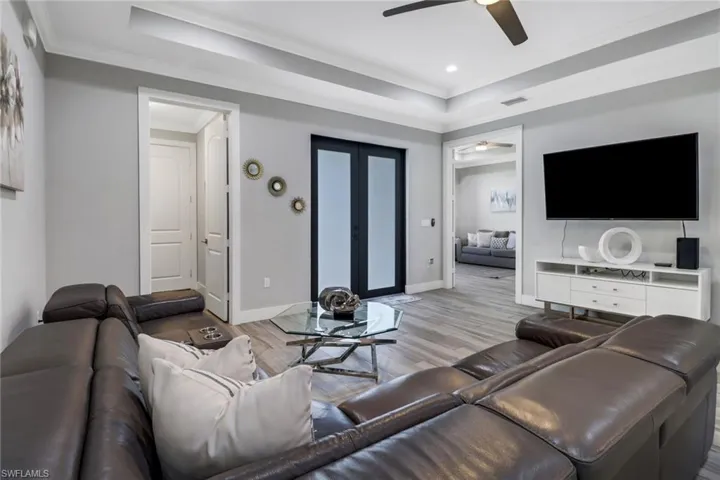 Living room with a raised ceiling, ornamental molding, light wood-type flooring, and ceiling fan