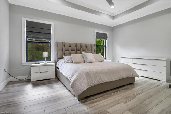 Bedroom with crown molding, a raised ceiling, light hardwood / wood-style flooring, and ceiling fan