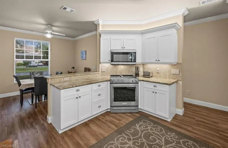 Kitchen with light stone countertops, appliances with stainless steel finishes, dark hardwood / wood-style floors, kitchen peninsula, and ceiling fan