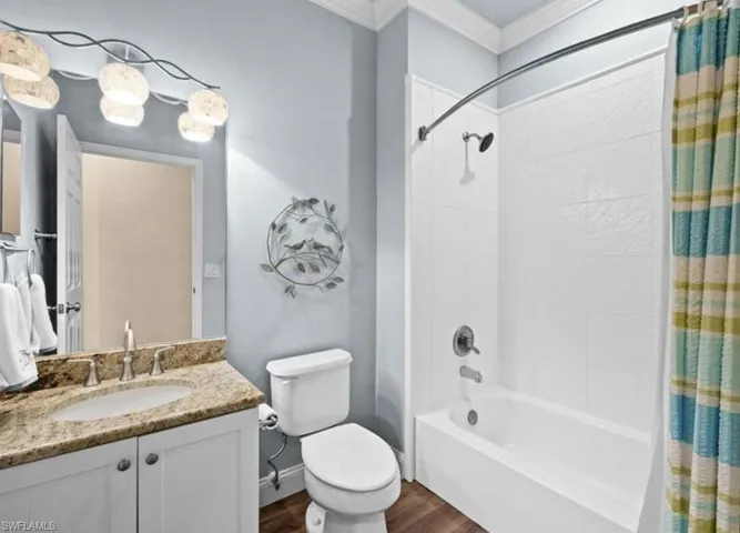 Full bathroom with shower / tub combo, ornamental molding, wood-type flooring, vanity with extensive cabinet space, and toilet