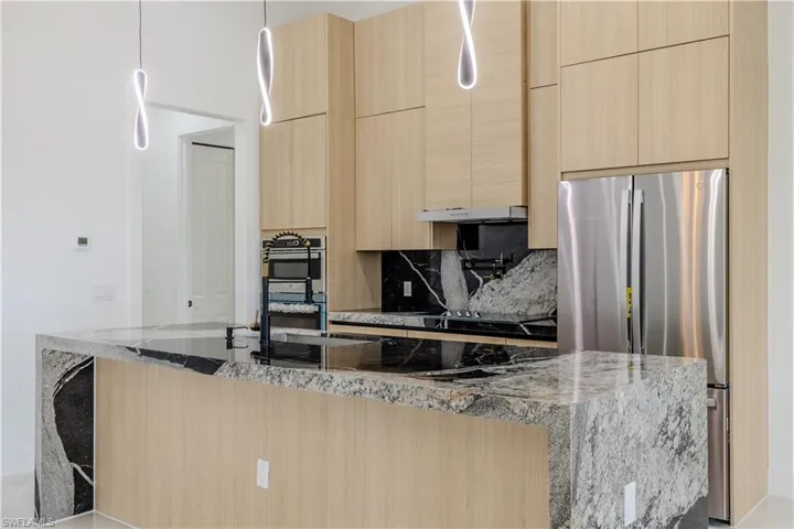 Kitchen featuring light brown cabinetry, dark stone counters, appliances with stainless steel finishes, and modern cabinets