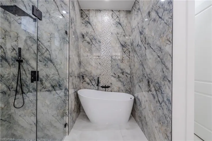 Full bath featuring a marble finish shower, a soaking tub, vanity, and tile patterned floors