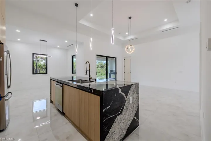 Kitchen featuring dark stone counters, a raised ceiling, pendant lighting, brown cabinets, and stainless steel appliances
