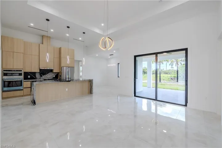 Kitchen with light brown cabinetry, decorative light fixtures, decorative backsplash, light stone counters, and an island with sink