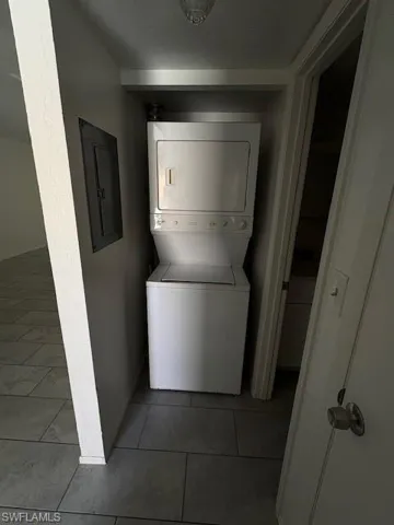 Laundry area featuring stacked washer / drying machine, electric panel, and light tile patterned flooring