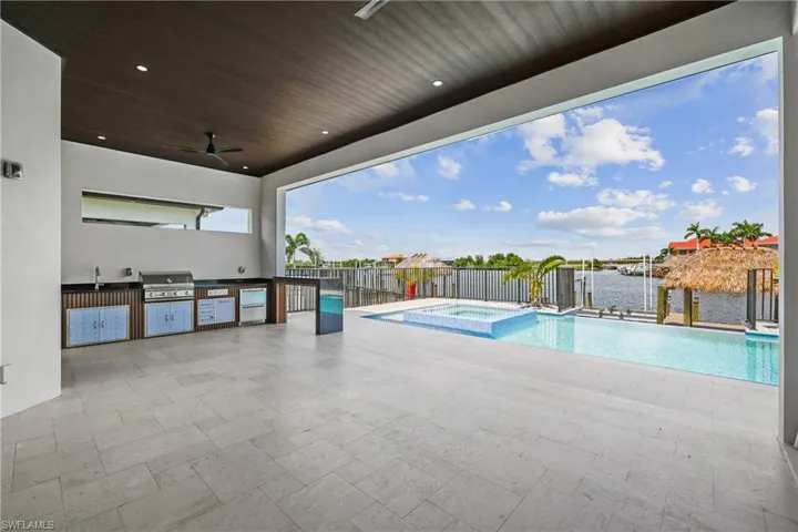 View of swimming pool featuring area for grilling, a pool with connected hot tub, a ceiling fan, a water view, and a patio area