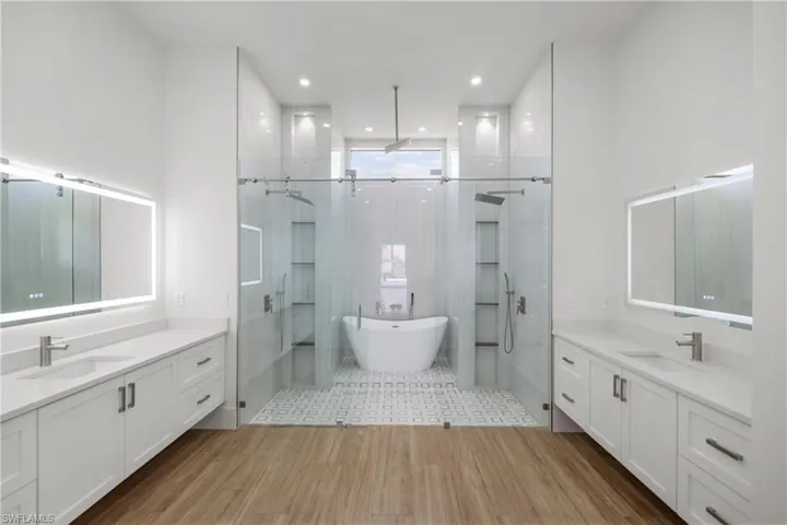 Full bathroom with wood finished floors, a shower stall, a soaking tub, and two vanities
