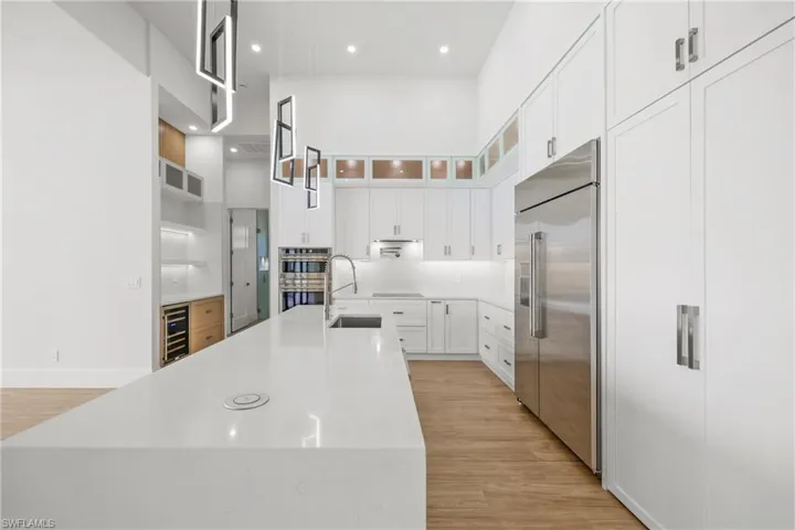 Kitchen featuring light wood-style floors, a towering ceiling, appliances with stainless steel finishes, light countertops, and white cabinets