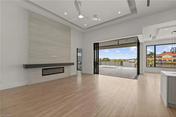 Unfurnished living room featuring light wood-type flooring, a fireplace, ceiling fan, recessed lighting, and a tray ceiling