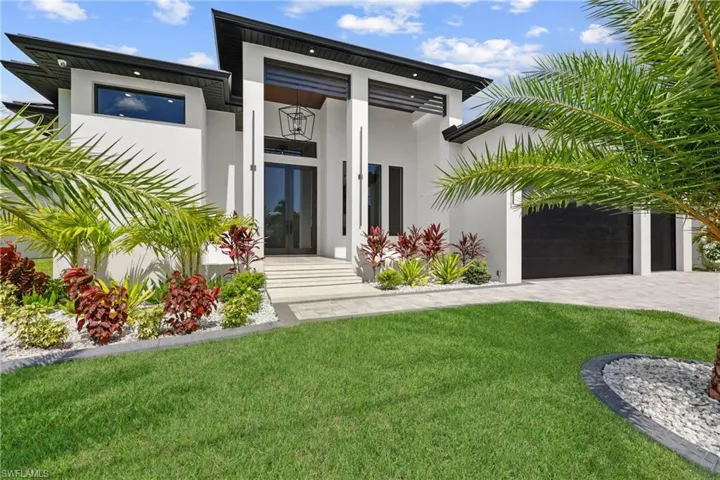 View of front facade with stucco siding, a front yard, french doors, decorative driveway, and an attached garage
