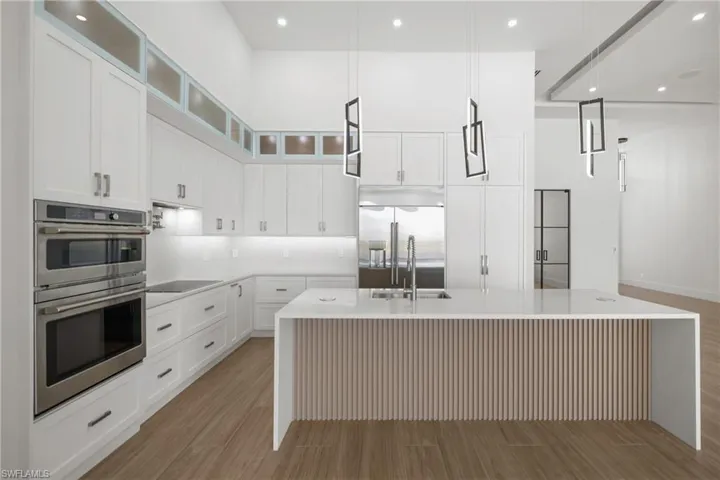 Kitchen featuring recessed lighting, appliances with stainless steel finishes, a kitchen island with sink, light wood finished floors, and a high ceiling