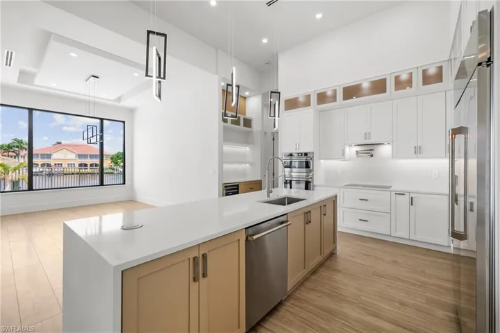 Kitchen featuring light wood-type flooring, appliances with stainless steel finishes, a kitchen island with sink, light countertops, and hanging light fixtures