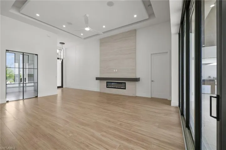 Unfurnished living room with light wood finished floors, a tray ceiling, recessed lighting, a fireplace, and a ceiling fan