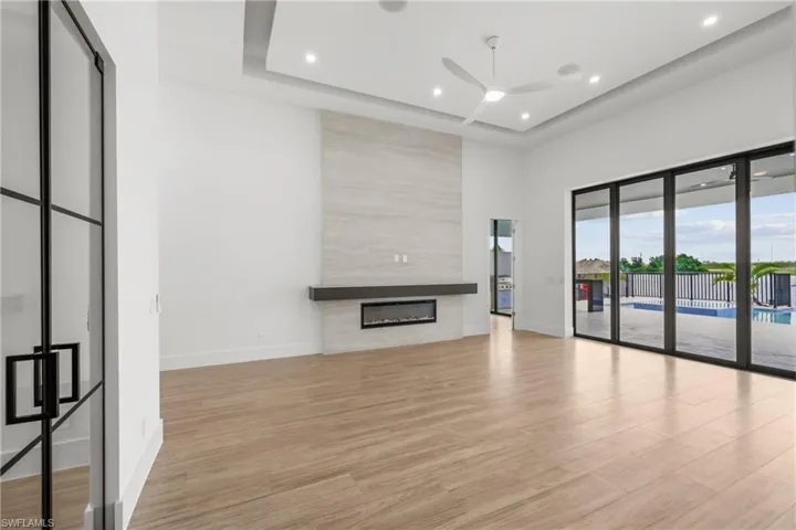 Unfurnished living room featuring light wood-style flooring, recessed lighting, a large fireplace, a tray ceiling, and ceiling fan
