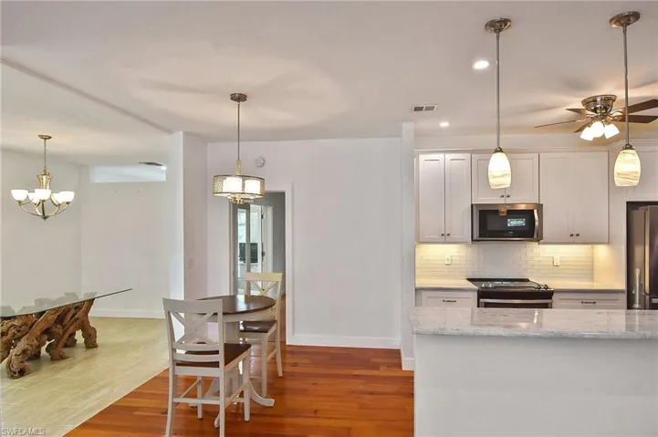 Kitchen featuring white cabinetry, stainless steel appliances, decorative backsplash, dark hardwood / wood-style flooring, and light stone countertops