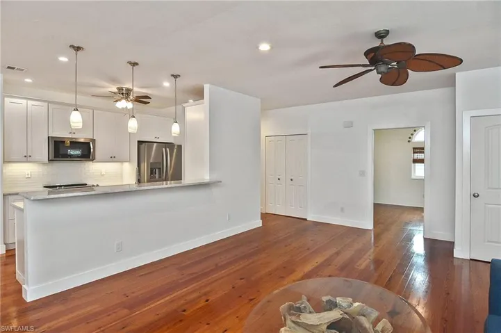 Kitchen with pendant lighting, white cabinets, dark hardwood / wood-style flooring, stainless steel appliances, and tasteful backsplash