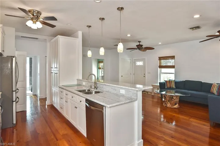 Kitchen featuring sink, white cabinetry, hanging light fixtures, appliances with stainless steel finishes, and light stone counters