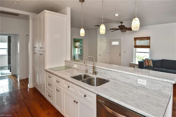 Kitchen with hanging light fixtures, a kitchen island with sink, sink, and white cabinetry