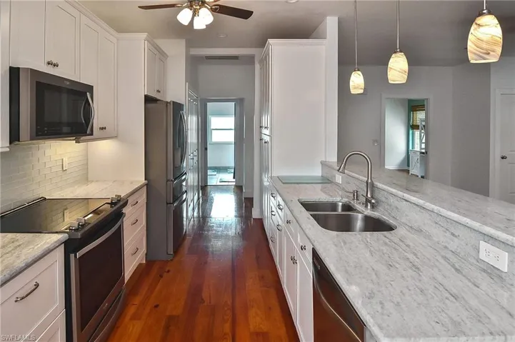 Kitchen featuring appliances with stainless steel finishes, light stone countertops, pendant lighting, white cabinets, and sink