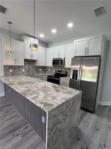 Kitchen featuring light wood-type flooring, a peninsula, visible vents, and appliances with stainless steel finishes