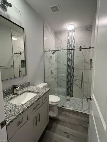 Full bathroom with a marble finish shower, toilet, visible vents, wood finished floors, and vanity