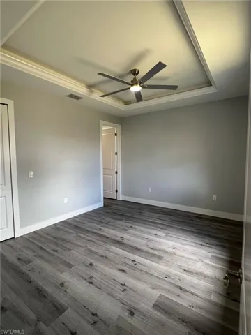 Empty room featuring dark wood finished floors, visible vents, baseboards, ceiling fan, and a raised ceiling