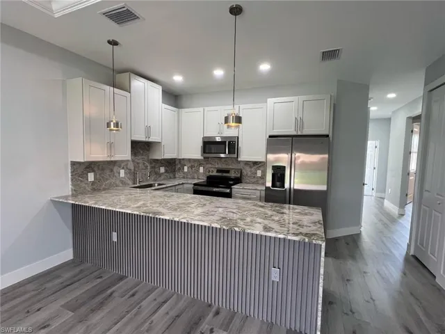 Kitchen featuring a peninsula, stainless steel appliances, visible vents, and baseboards