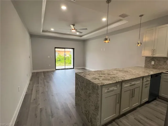 Kitchen with a tray ceiling, black dishwasher, light stone counters, a peninsula, and wood finished floors