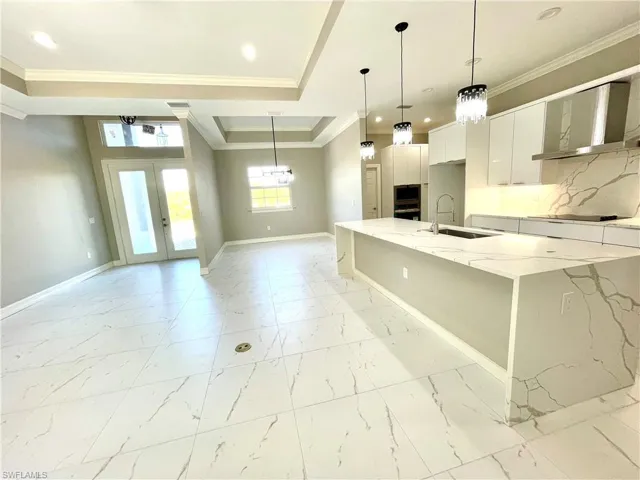 Kitchen with light stone counters, wall chimney range hood, decorative light fixtures, french doors, and white cabinetry