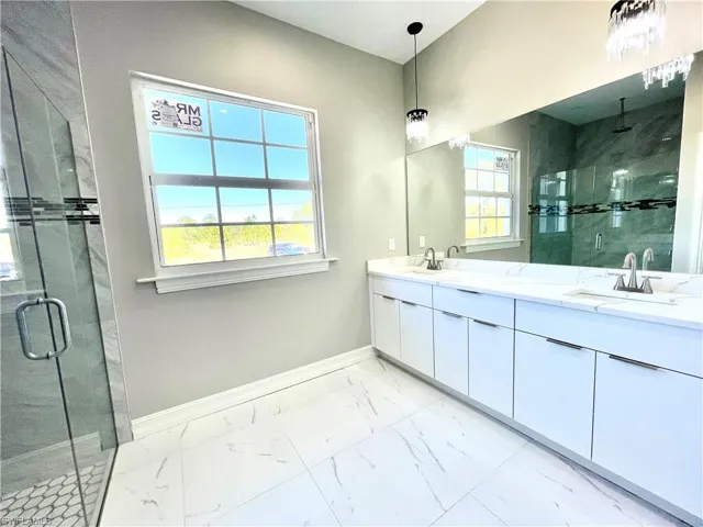 Bathroom with a shower stall, double vanity, and light marble finish flooring